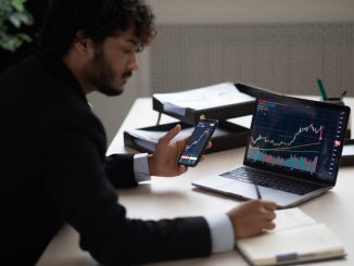 Smart focused Indian broker investor, stock trader using smartphone and laptop to analyze and invert in the financial market of cryptocurrencies, buy or sell crypto coins, planning strategy